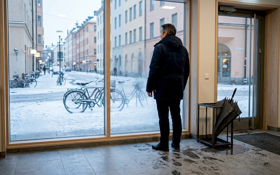 Man looks out Stockholm apartment lobby in winter